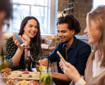 technology, lifestyle and people concept - happy friends with smartphones taking picture of food at bar or cafe